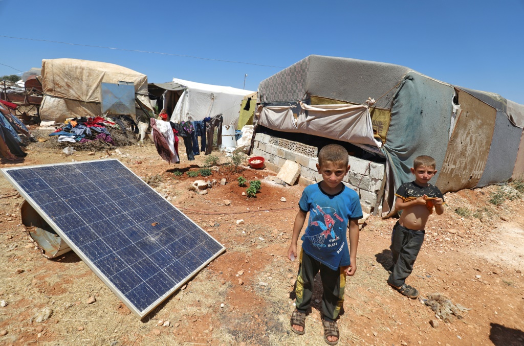 Children stand near a solar panel at a camp for Syrians displaced by conflict, near the Syrian border with Turkey in the rebel-held northern part of Idlib province