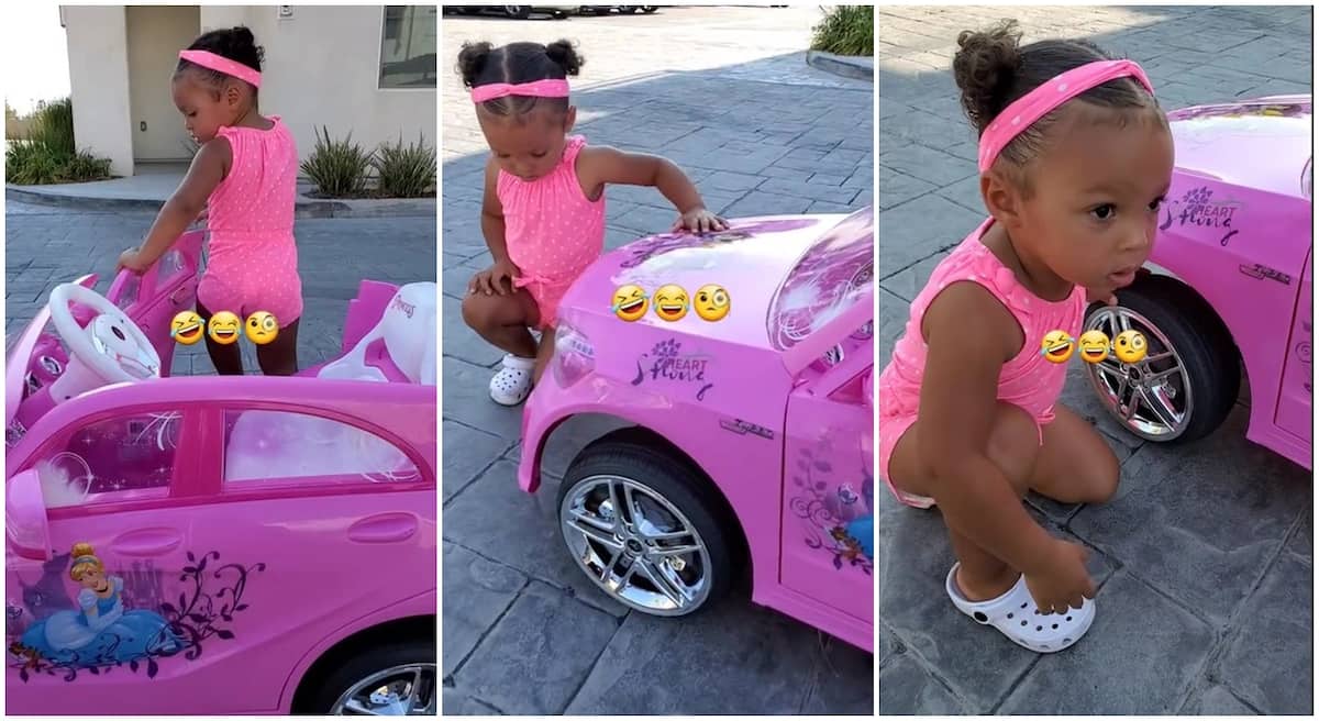 Black toddler in pink dress, squatting close to a pink toy car.