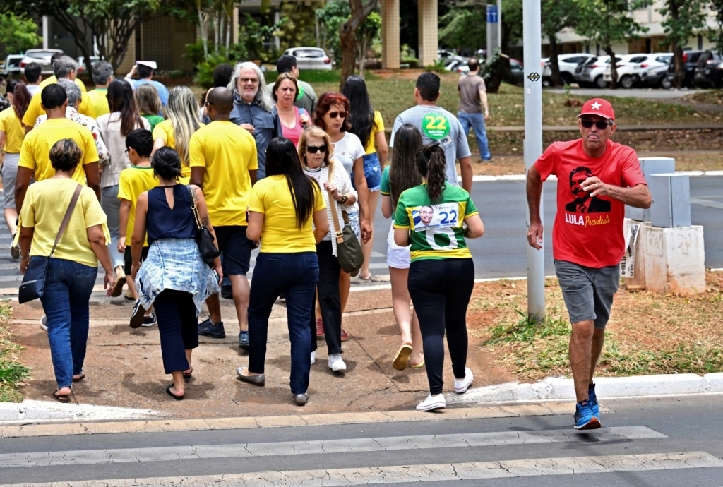 A supporter (R) of former president Luiz Inacio Lula da Silva walks in the other direction to supporters of president and election rival Jair Bolsonaro, as they cross a street in Brasilia, on October 30, 2022, during the presidential run-off
