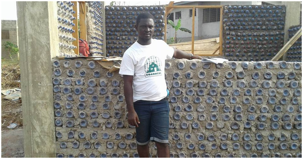 Man stands by a house he is building with plastic bottles