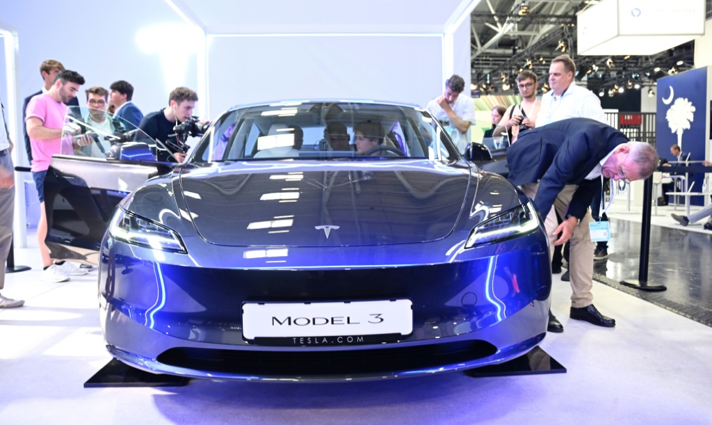Visitors inspect a Tesla model 3 car on display at the International Motor Show held in Munich, southern Germany, on September 4, 2023
