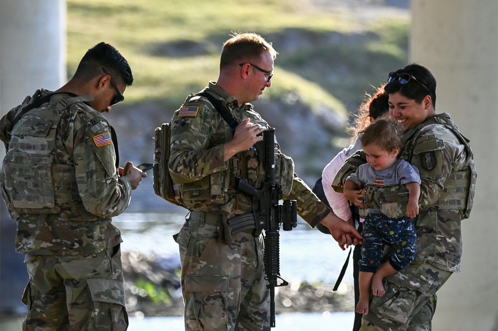 Border patrol and National Guard troops play with a migrant child who crossed into Texas