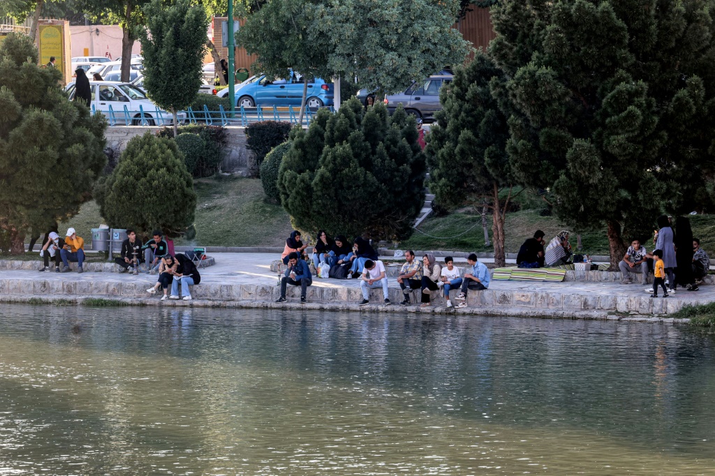 A file picture shows people sitting along the bank of the Zayandeh Rood river on May 15, 2022 in Iran's central city of Isfahan -- the river has been drying out, but families seek out riversides and other cooler areas to relax during the summer