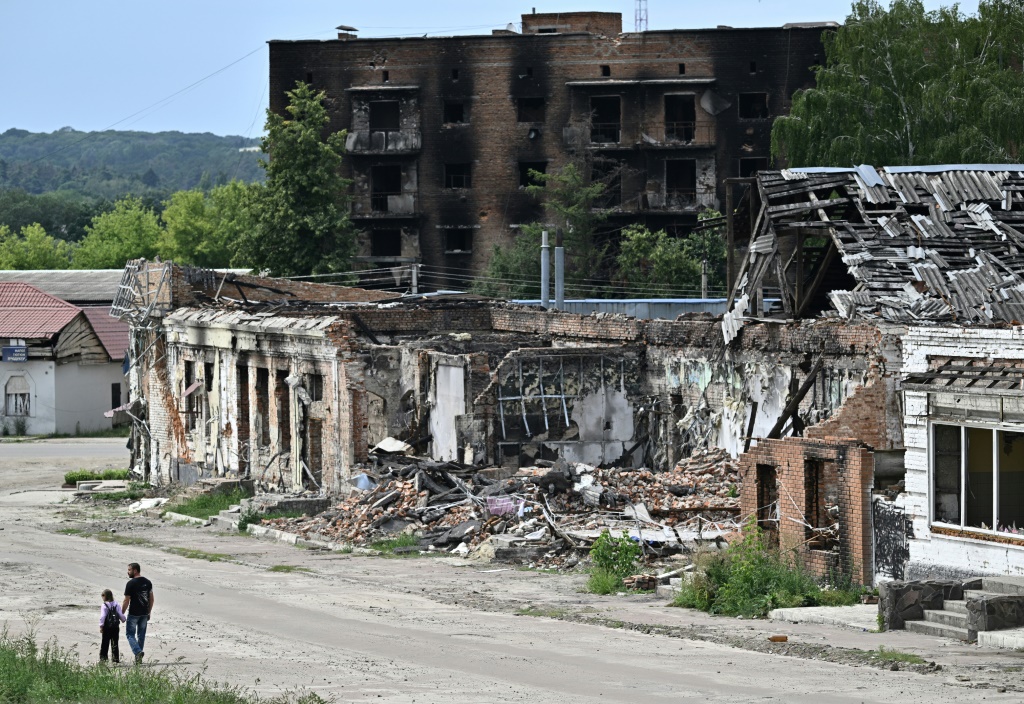 Pedestrians walk past destroyed buildings in the city of Trostyanets