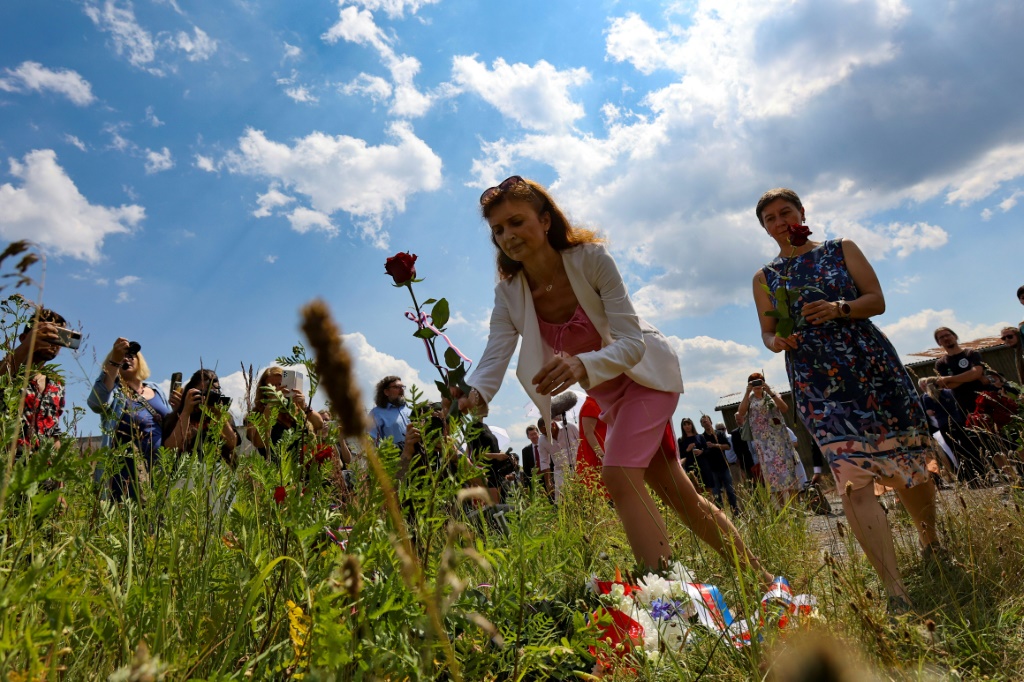 People lay roses on a field in front of the Czech pig farm built on the site of a WWII concentration camp for the Roma