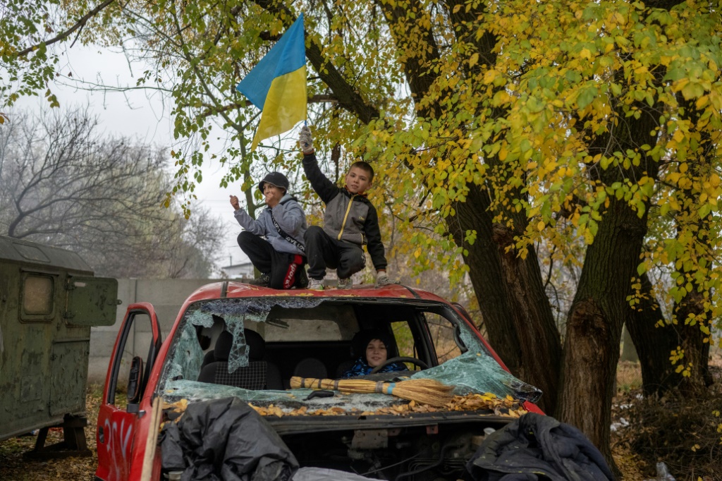 A young boy waves a Ukrainian flag from a destroyed car at a former Russian checkpoint at the entrance to Kherson