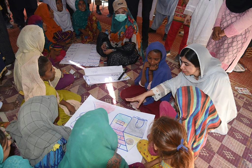 This handout picture taken and released by Chief Minister House Office of Sindh Province on October 12, 2022 shows Nobel Peace laureate Malala Yousafzai (R) speaking with flood-affected children at a makeshift school in Johi, Dadu district of Sindh province