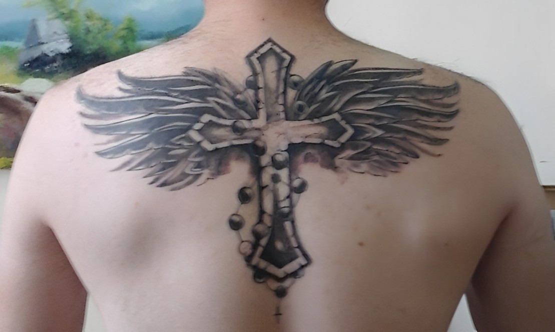 A man has a cross with wings tattoo on his upper back
