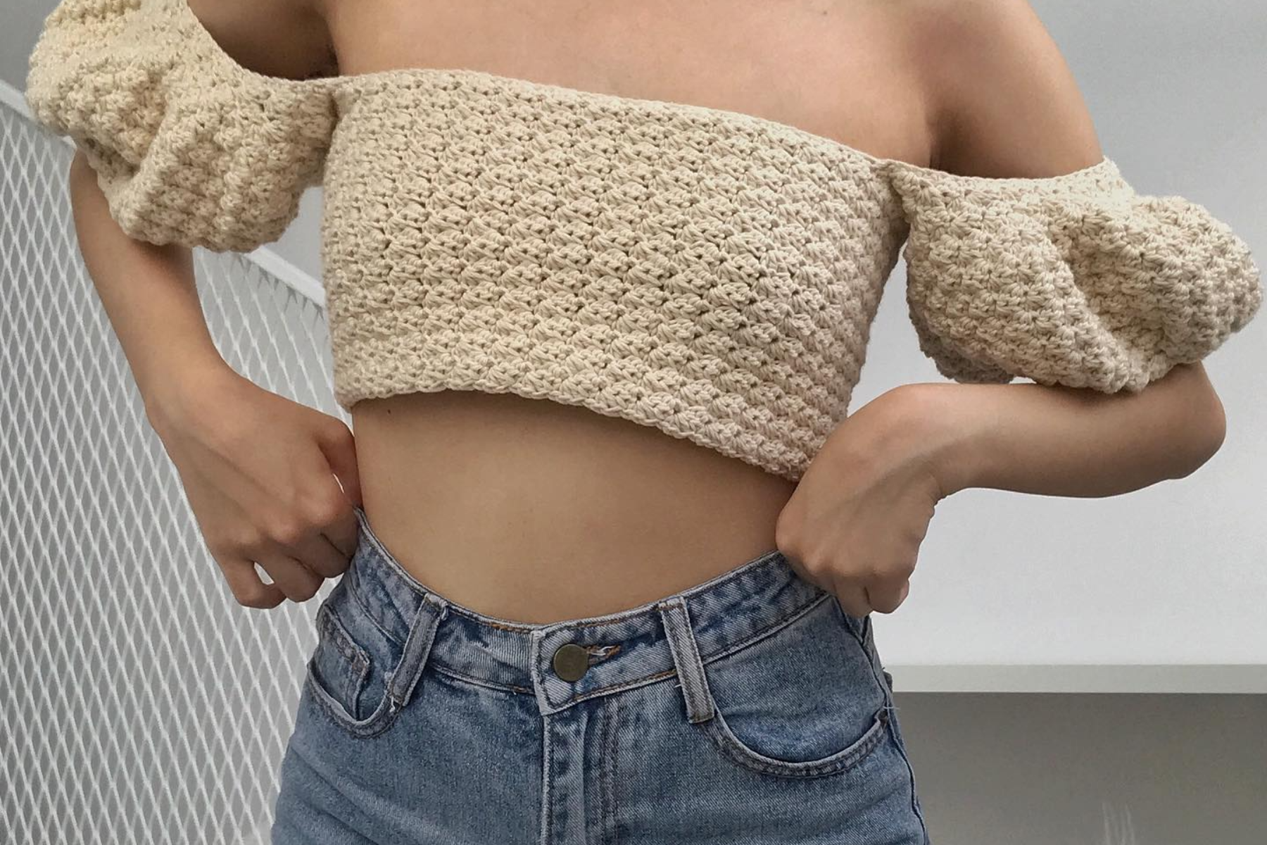 A lady is wearing a crochet crop top with a pair of jeans