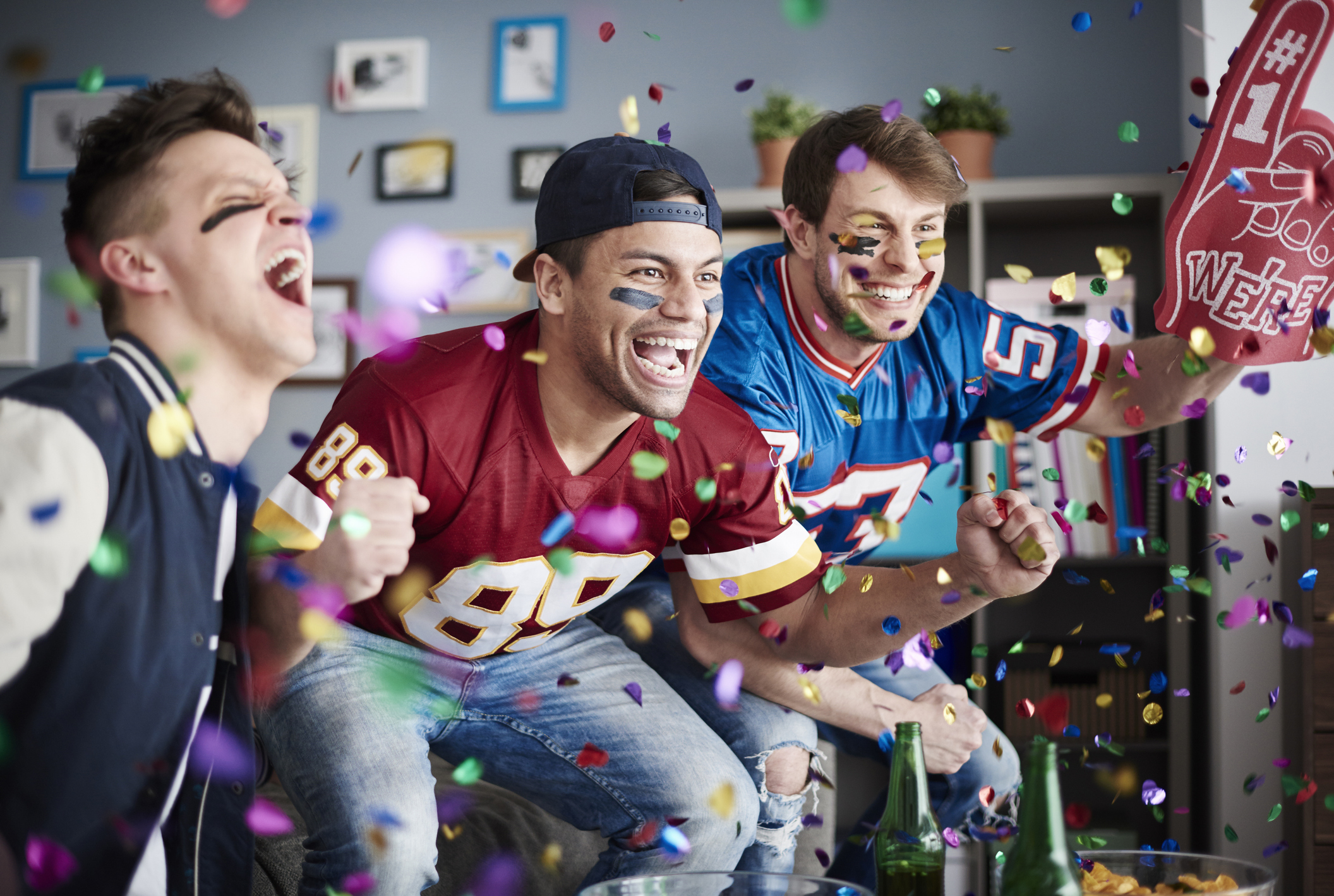 Three American football fans celebrate a win among falling confetti.