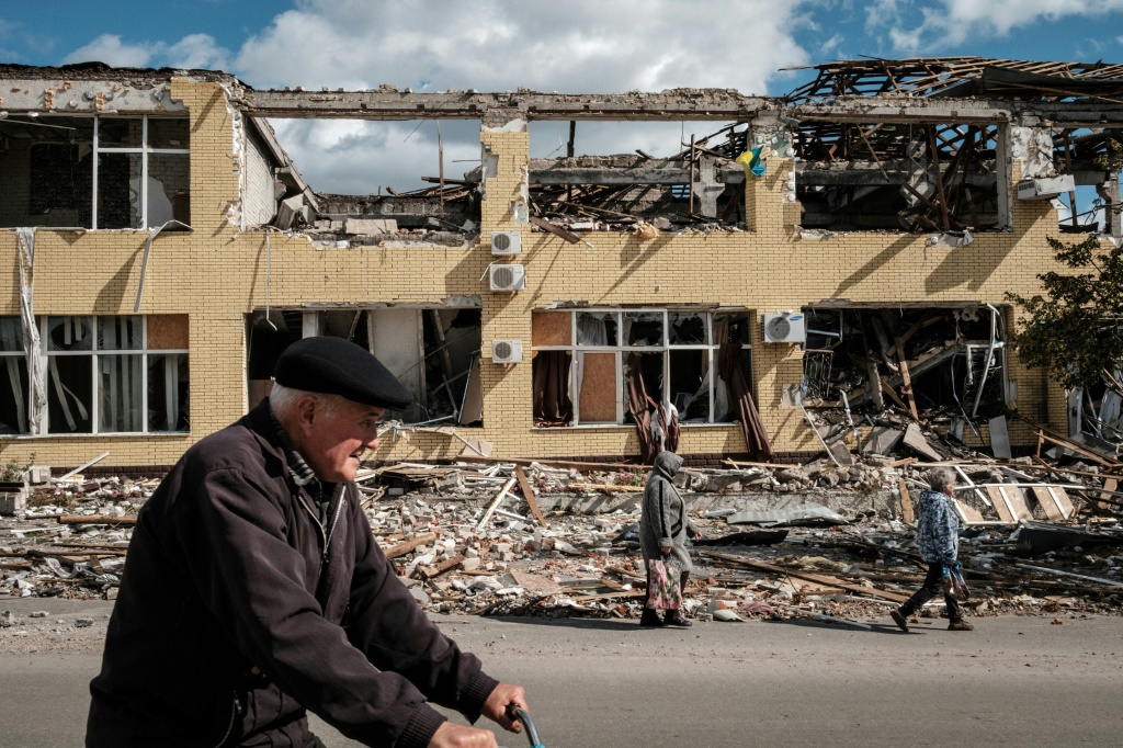 People walk past a destroyed building in Kupiansk, Ukraine