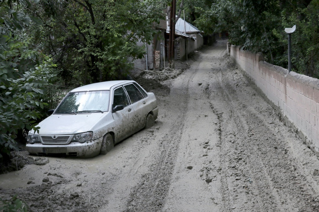 A car partially buried in mud on a road in the Firouzkouh area