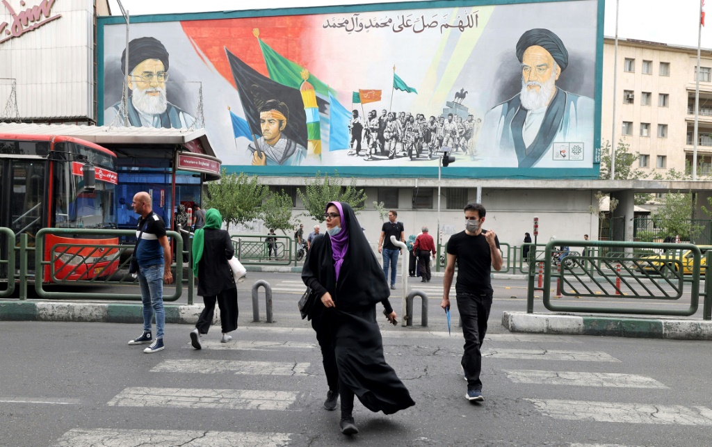 Iranians pass a billboard showing Iran's supreme leader Ayatollah Ali Khamenei and Ayatollah Ruhollah Khomeini (R) in Tehran, before the anti-regime protest movement began in September 2022