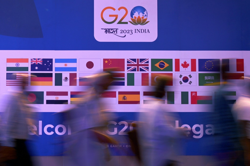 People walk past a banner with flags of countries participating in the G20 summit in New Delhi