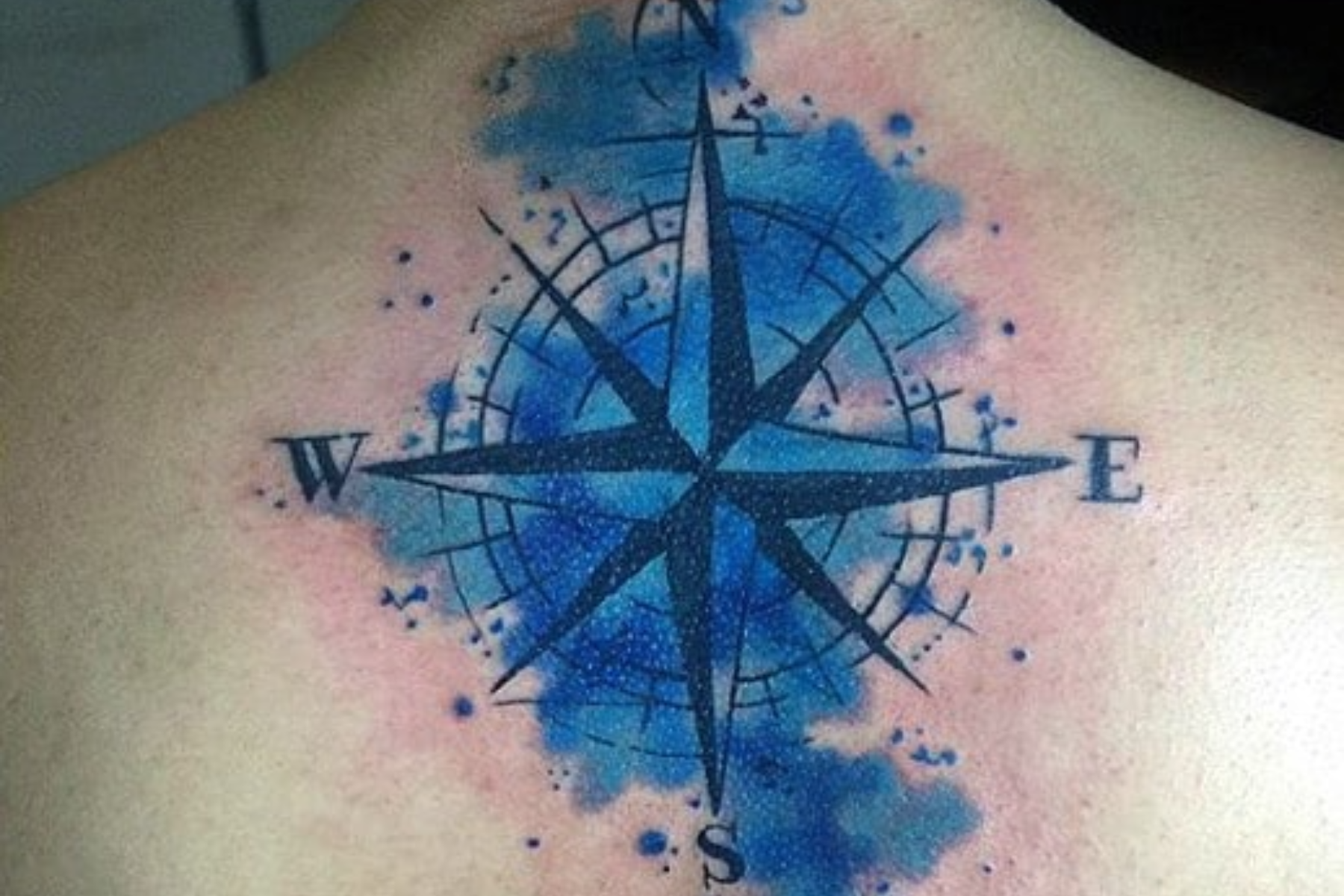 A man has a watercolour compass tattoo at the back