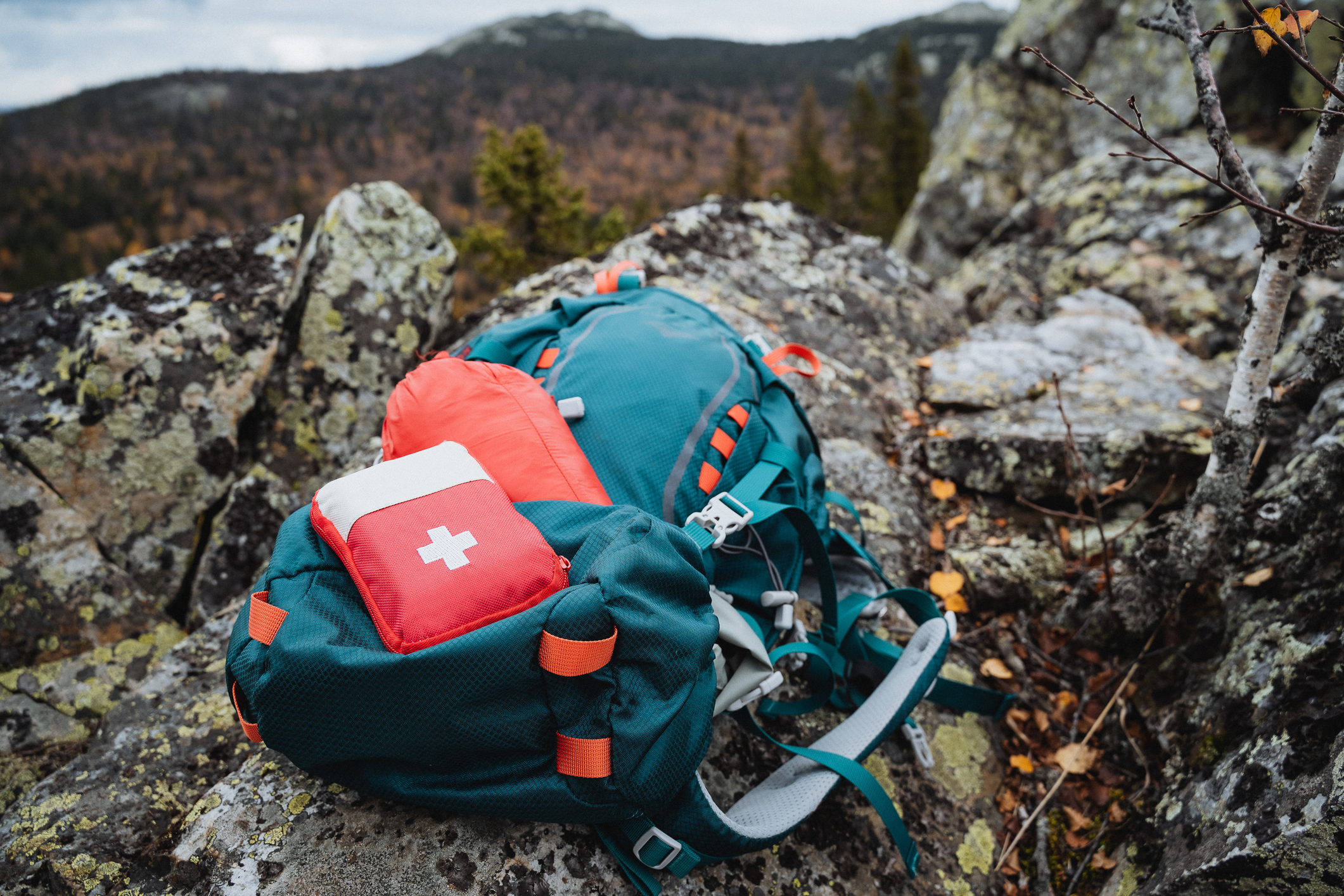 A red hiking first aid kit is on a backpack on the mountains.