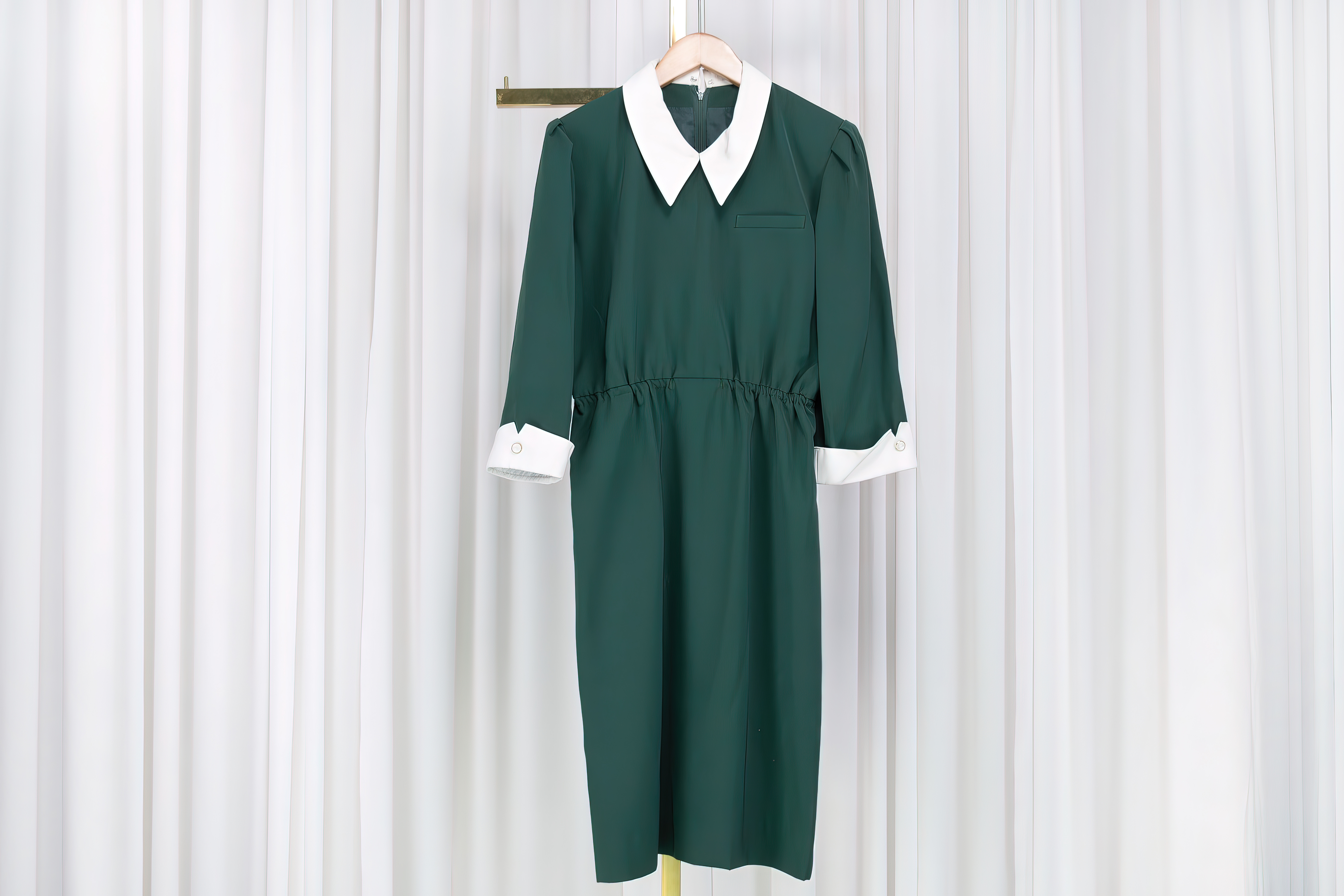 A green dress is hanging from a coat hanger in front of a white curtain