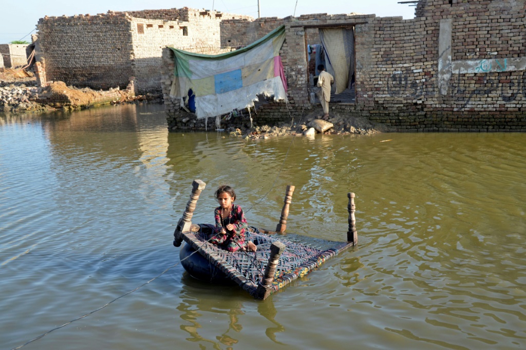 A girl sits on a cot as she crosses a flooded street at Sohbatpur in Jaffarabad district of Balochistan province on October 4, 2022