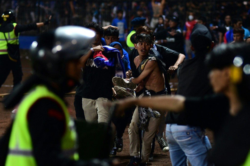 A group of people carry a man off the field at Kanjuruhan stadium on the night of the disaster