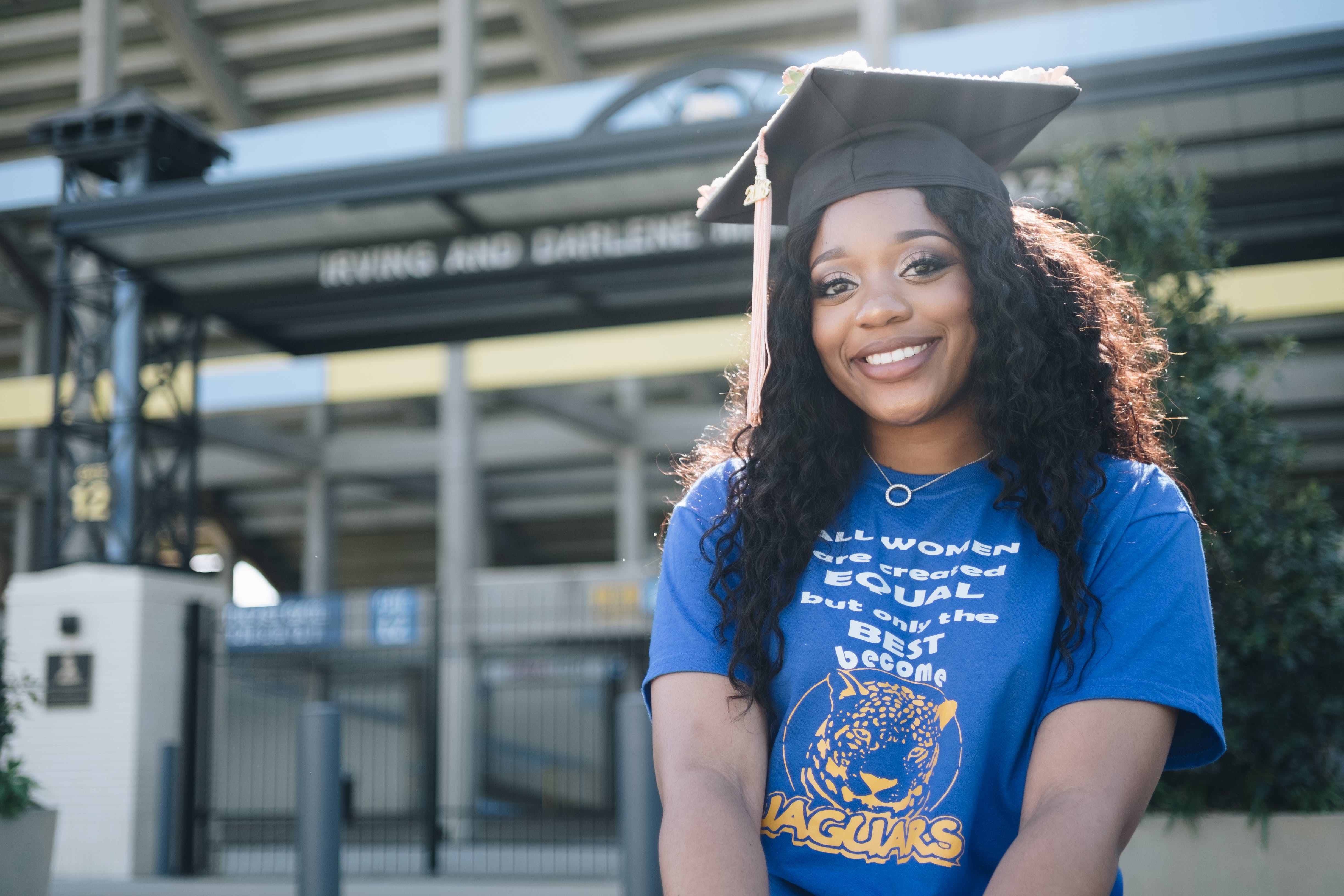 A lady is wearing a black graduation cap and a blue tee with writings