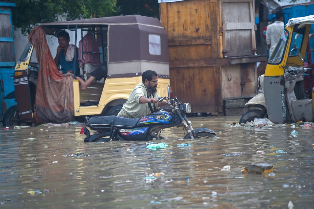 A man pushes his motorbike through a flooded street after heavy monsoon rain in Karachi