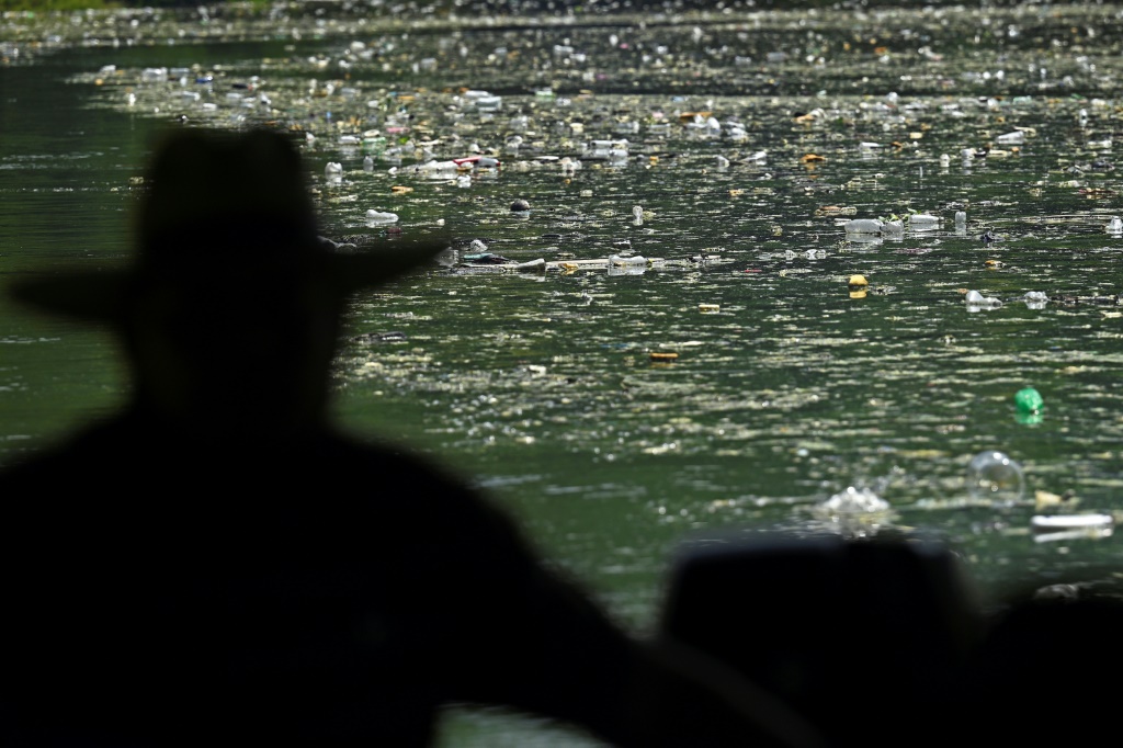A fisherman looks out over the carpet of plastic waste covering the Cerron Grande reservoir in Potonico, El Salvador