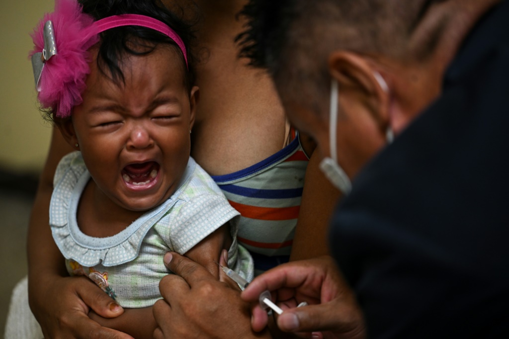 A girl accompanied by her mother receives a dose of measles and rubella vaccine from medical personnel at a community health center in the Lidice neighborhood in Caracas