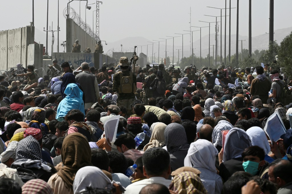 Afghans gather on a roadside near the military part of the airport in Kabul on August 20, 2021, hoping to flee from the country after the Taliban's military takeover of Afghanistan