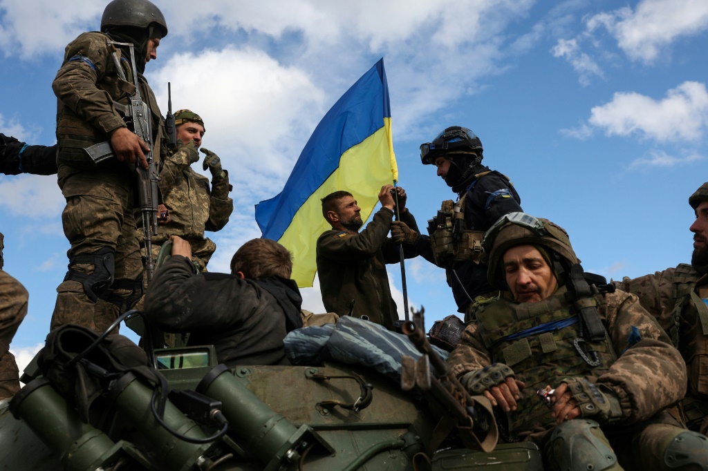 Ukrainian soldiers fix a national flag atop an armoured personnel carrier near Lyman in the Donetsk region