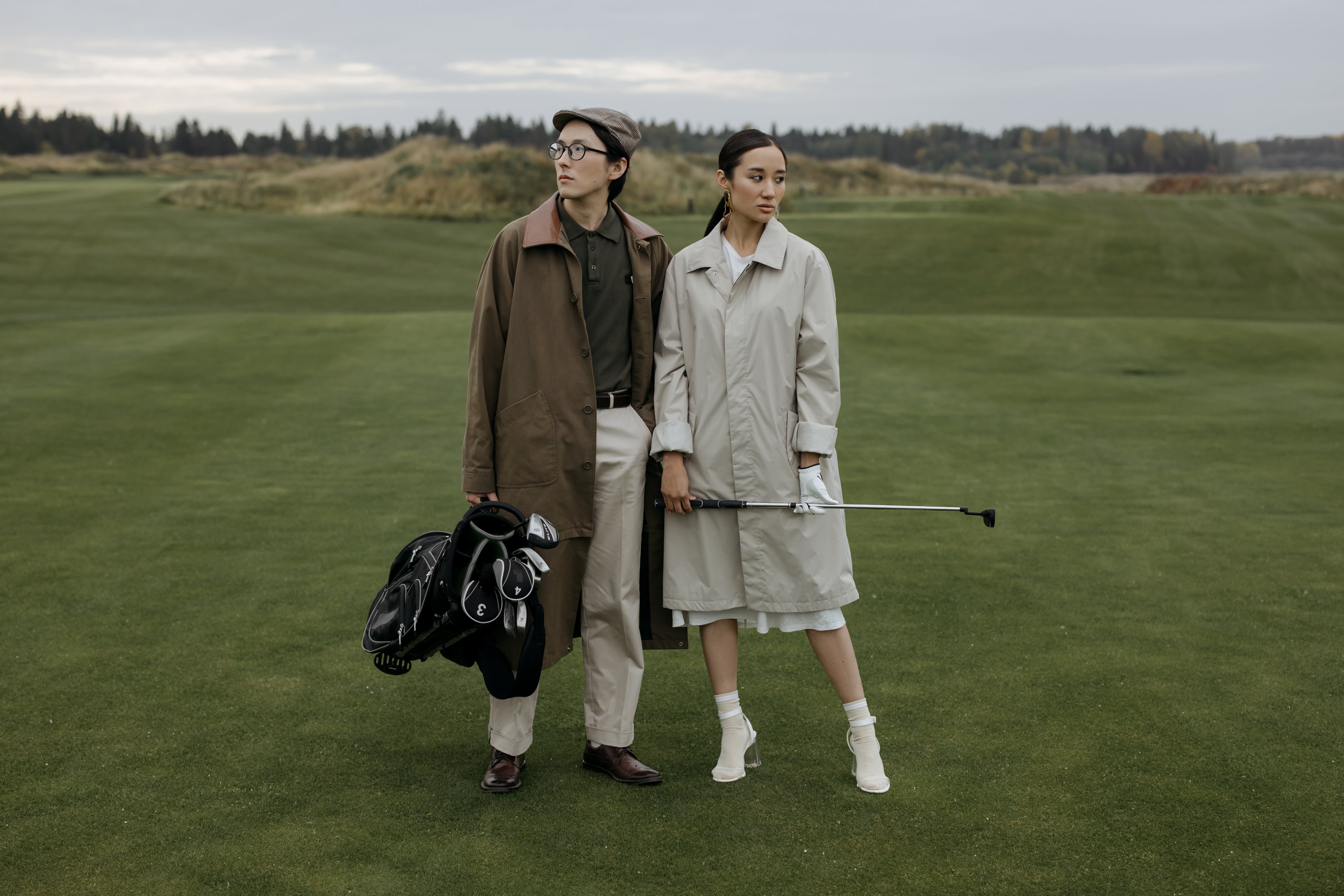 A man and a woman in coats posing at a golf course