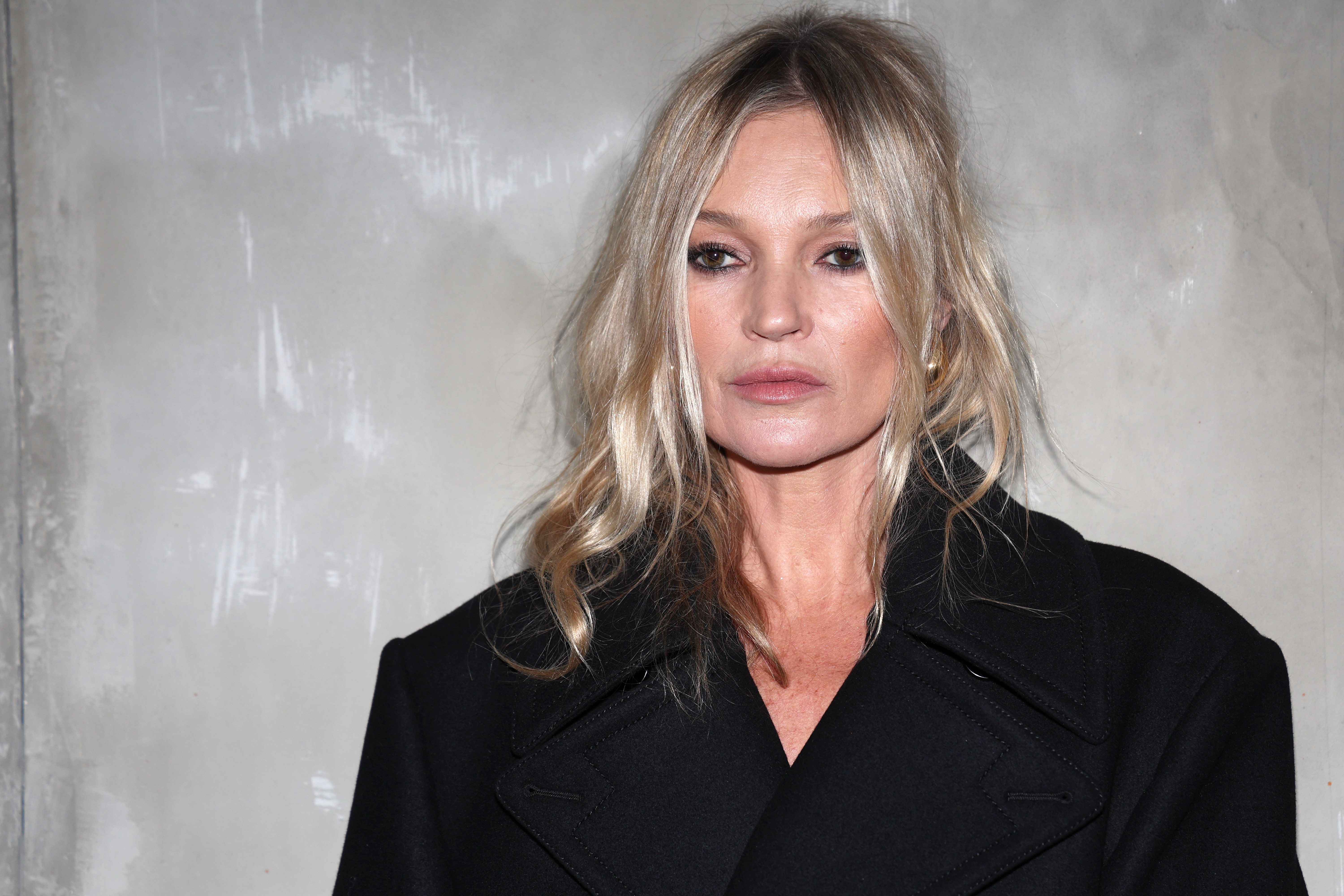 Kate Moss, in black, poses against a grey background in Milan, Italy